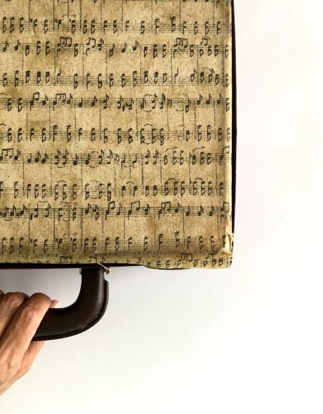 Hand holding a vintage clarinet case with music notes printed.